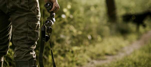a man wear a hunting bib and hold a binoculars in the wild